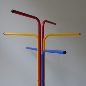 May include: A colorful coat rack with four arms, each a different color: red, yellow, blue, and a fourth arm that is red and yellow. The arms are all curved and have black tips.