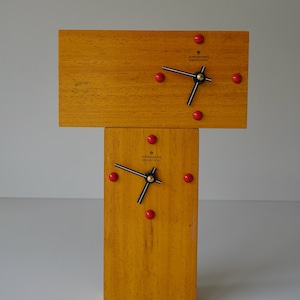 May include: A wooden clock with a T-shaped design. The clock face is white with black hands and red dots for the numbers. The clock face says "JUNGHANS electronic".
