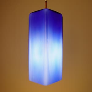 May include: A modern, rectangular pendant light fixture with a gradient blue and white color scheme. The light hangs from a white cord and a copper-colored fixture. The light's shape is a square prism.