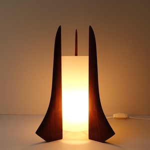 Könnte beinhalten: Eine moderne Tischlampe aus der Mitte des Jahrhunderts mit einem weißen Schirm und einem dunklen Holzsockel. Der Sockel ist in Form von zwei Flügeln gestaltet.