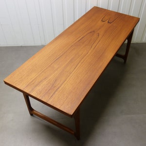 Può includere: Un tavolino da caffè rettangolare in legno con finitura in legno naturale. Il tavolo ha un design semplice e moderno di metà secolo con un piano rettangolare e quattro gambe.