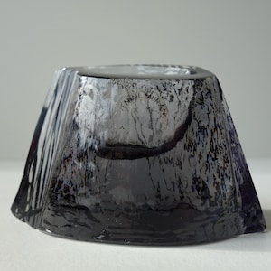 Pode incluir: Um cinzeiro de vidro cinza escuro com uma superfície texturizada e uma depressão circular no centro. O cinzeiro é marcado com o texto "ENNI  NAUKA  ANN"