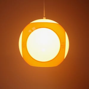 May include: A white and orange pendant light with a circular design. The light is on and illuminating the room.