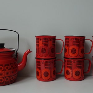 Puede incluir: Un juego de tazas de esmalte rojo y una tetera a juego con diseños geométricos negros y naranjas. Las tazas tienen interiores blancos y bordes negros.