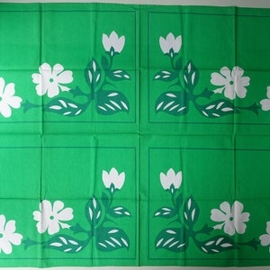 May include: A green fabric with a repeating pattern of white flowers and green leaves. The fabric is divided into four squares.