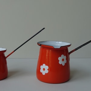 Könnte beinhalten: Zwei orangefarbene Emaille-Kaffeekannen mit weißen Blumenmustern und schwarzen Griffen. Die kleinere Kanne hat einen kürzeren Griff.