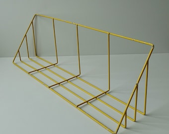 May include: A yellow metal wall shelf with a triangular design and four shelves. The shelf is made of thin metal and has a simple, modern design.