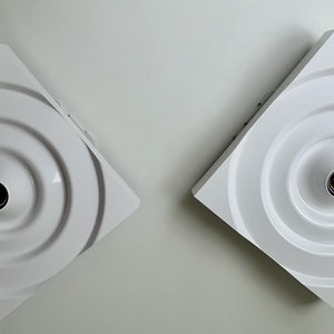 Puede incluir: Dos apliques de pared cuadrados blancos con un dise&ntilde;o circular y una sola bombilla en el centro de cada uno.