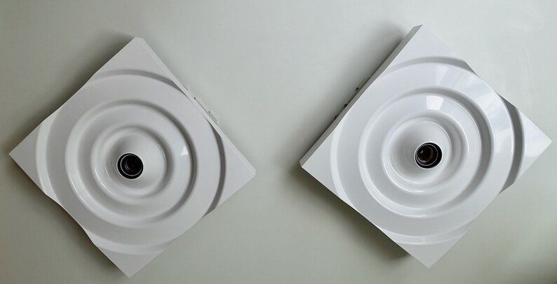 Puede incluir: Dos apliques de pared cuadrados blancos con un dise&ntilde;o circular y una sola bombilla en el centro de cada uno.