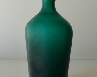 May include: A teal blue glass bottle with a frosted finish and a light green glass stopper. The bottle has a rounded body and a slightly flared neck.