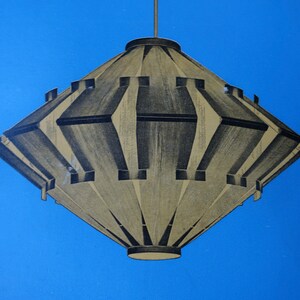 Könnte beinhalten: Eine geometrische Pendelleuchte in Diamantform in Gold und Schwarz. Die Leuchte hängt an einer Decke vor blauem Hintergrund.