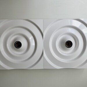 Puede incluir: Una l&aacute;mpara de pared blanca con dos bombillas circulares empotradas. La l&aacute;mpara tiene un dise&ntilde;o moderno y minimalista.