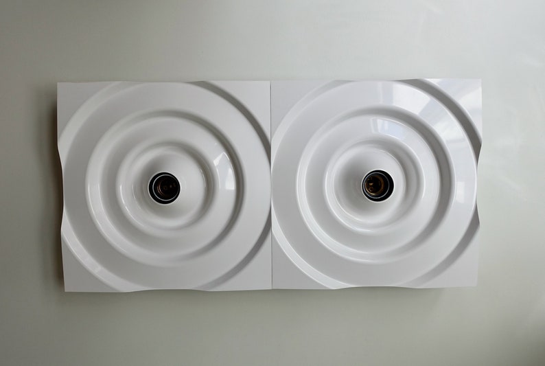 Puede incluir: Una l&aacute;mpara de pared blanca con dos bombillas circulares empotradas. La l&aacute;mpara tiene un dise&ntilde;o moderno y minimalista.