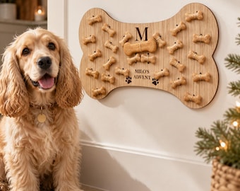 May include: A light-colored wooden wall-mounted dog treat advent calendar shaped like a large bone. It features the letter M, the text MILO'S ADVENT, and two paw prints. Small bone-shaped treats are attached to the board in rows.