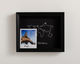 May include: Black picture frame with a white line drawing of a world map and the word "Adventures" underneath. A photo of the Eiffel Tower in Paris is in the frame with the word "Paris" underneath.
