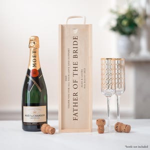 May include: Wooden gift box with a champagne bottle, two champagne flutes, and a cork. The box is engraved with the text "Father of the Bride" and a personalized message.