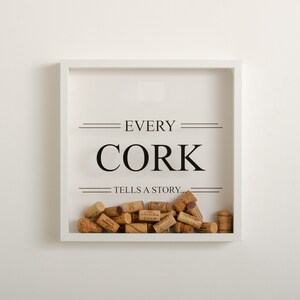 Peut inclure: Un cadre blanc avec le texte "EVERY CORK TELLS A STORY..." et une collection de bouchons de vin à l'intérieur.