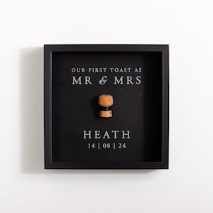 May include: Black framed shadow box with a champagne cork, the text "Our First Toast as Mr & Mrs Heath 14 | 08 | 24" is printed in white.