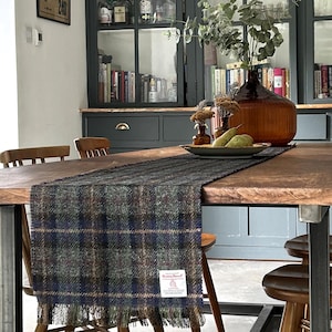 以下が含まれることがあります： 格子柄のテーブルランナーがかけられた木製のダイニングテーブル。テーブルは、古材を使用した素朴な風合いで、黒い金属製の脚で支えられています。テーブルの周りに4つの椅子があり、そのうち2つが画像に写っています。テーブルには、フルーツボウルと緑色の花瓶が置かれています。