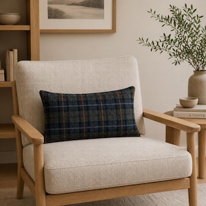 Op de afbeelding: Een rechthoekig sierkussen met een ruitpatroon in blauw, groen en bruin ligt op een crèmekleurige fauteuil. Het kussen voegt een vleugje kleur en textuur toe aan de neutrale zitting. De stoel heeft een houten frame.