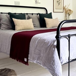 May include: A black metal bed frame with a grey linen duvet and a burgundy throw blanket. The bed is styled with pillows in various shades of green and beige.