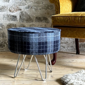 May include: A round, blue and black plaid ottoman with silver hairpin legs. The ottoman is sitting on a wooden floor.