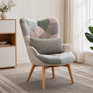 Op de afbeelding: Een patchwork fauteuil met een hoge rugleuning en houten poten. De stoel heeft een mix van neutrale kleuren, waaronder beige, grijs en groen, gerangschikt in een geometrisch patroon. Een grijs rechthoekig kussen ligt op de zitting.