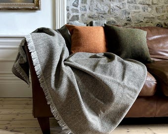 May include: A brown leather couch with a gray and white herringbone throw blanket draped over it. There are three throw pillows on the couch, one orange, one green, and one brown.