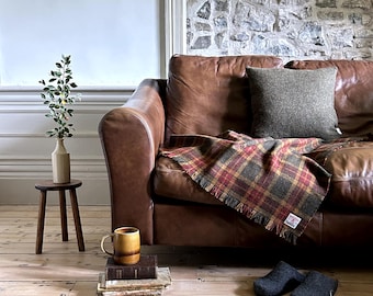 Peut inclure: Un canapé en cuir marron avec une couverture en plaid et un coussin marron. Le canapé est dans un salon avec un sol en bois et un petit tabouret en bois avec un vase de verdure.