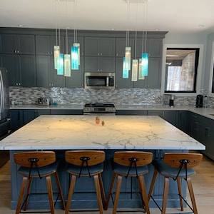 May include: A kitchen island with a white marble worktop and four wooden bar stools. The island is lit by a modern light fixture with blue glass pendants.