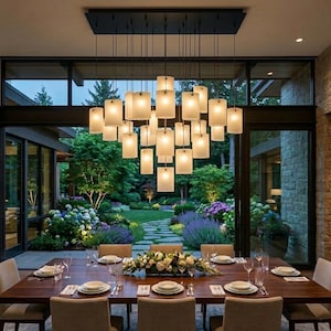 May include: A modern dining room with a large wooden table set for a meal. Above the table hangs a rectangular chandelier with multiple rectangular, frosted glass shades. Large windows offer a view of a lush garden.