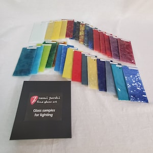 May include: A collection of glass samples for lighting, arranged in a semi-circle. The samples are in various colors, including red, blue, green, yellow, and clear. The samples are labeled with the name "Zromi Zarchi Fine Glass Art".