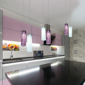 May include: A modern kitchen with a black worktop and white cabinets. Five rectangular glass pendant lights hang from the ceiling, with two purple and three blue glass shades.