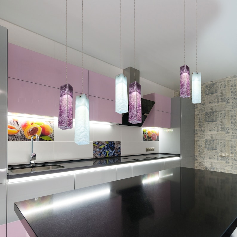 May include: A modern kitchen with a black worktop and white cabinets. Five rectangular glass pendant lights hang from the ceiling, with two purple and three blue glass shades.