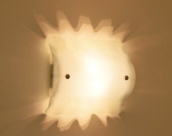 May include: A wall-mounted light fixture featuring a curved, translucent white glass shade with a wavy, scalloped edge. The shade is secured by two small, circular metallic fasteners, emitting a warm, soft glow that casts distinct shadows.