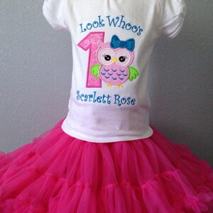 Puede incluir: Una camiseta blanca con un n&uacute;mero uno rosa y un b&uacute;ho con un lazo azul. El texto "Look Who's" est&aacute; por encima del n&uacute;mero y "Scarlett Rose" por debajo. La camiseta se combina con una falda de tul rosa.