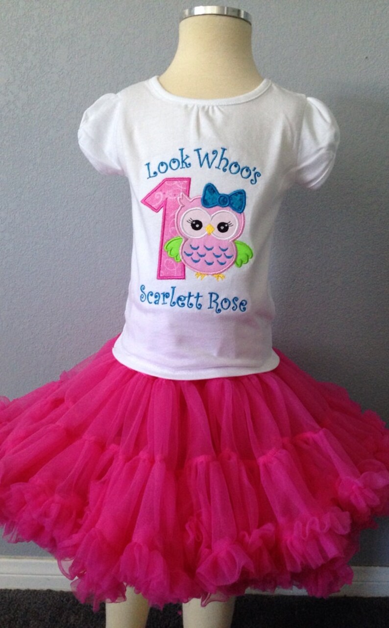 Puede incluir: Una camiseta blanca con un n&uacute;mero uno rosa y un b&uacute;ho con un lazo azul. El texto "Look Who's" est&aacute; por encima del n&uacute;mero y "Scarlett Rose" por debajo. La camiseta se combina con una falda de tul rosa.