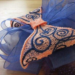 May include: A peach-coloured bow with black embroidery and a swirl pattern, on top of a blue tulle fabric.