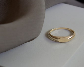 May include: A gold signet ring with a smooth, oval-shaped top.