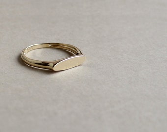 May include: A gold signet ring with a flat, oval-shaped top. The ring is simple and elegant.