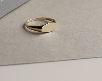 May include: A gold signet ring with a smooth, oval-shaped top.