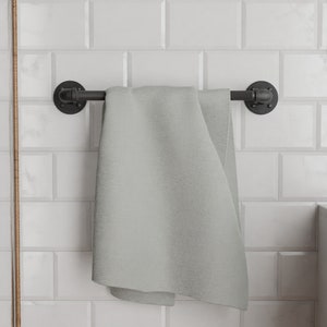 May include: A grey towel hanging on a black metal towel rail with industrial pipe fittings. The towel rail is mounted on a white tiled wall.
