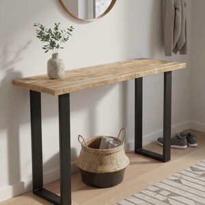 May include: A wooden console table with black metal legs, a round mirror, and a woven basket. A vase with greenery sits on the table. A rug with a geometric pattern and a coat rack with a grey jacket complete the entryway.