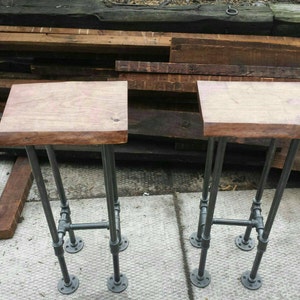 May include: Two wooden bar stools with black metal pipe legs. The stools have a natural wood finish and are made with a live edge design.
