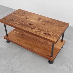 May include: A two-tiered wooden coffee table with a rustic brown finish. The table has a black metal pipe frame and legs.