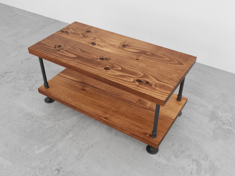 May include: A two-tiered wooden coffee table with a rustic brown finish. The table has a black metal pipe frame and legs.