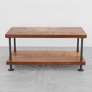 May include: A two-tiered wooden table with a dark brown finish and black metal pipe legs. The table has a rectangular top and bottom shelf.