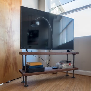 May include: A flat screen television sits on a wooden shelf with black metal pipe legs. The shelf has books and other items on it.