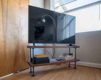 May include: A flat screen television sits on a wooden shelf with black metal pipe legs. The shelf has books and other items on it.