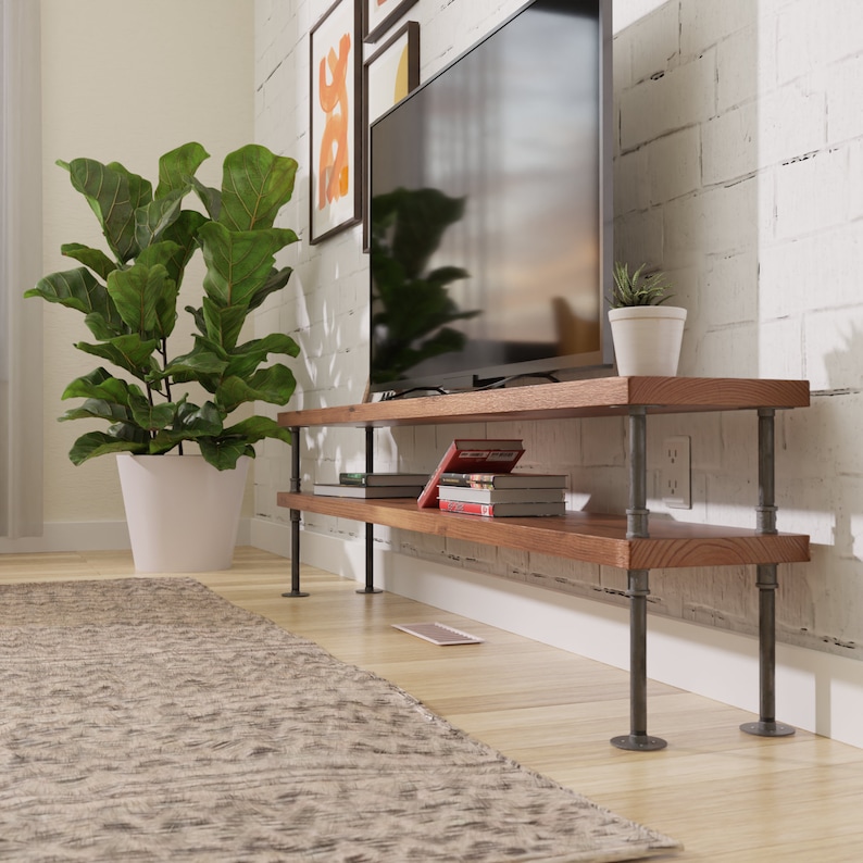 Puede incluir: Una estanter&iacute;a de madera de dos niveles con patas de tubo de metal negro. La estanter&iacute;a tiene libros y un televisor. La estanter&iacute;a est&aacute; delante de una pared de ladrillo blanco.